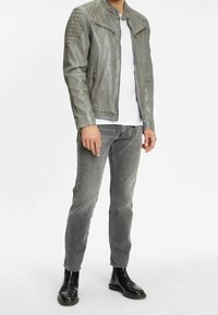 Grå læderjakke med lynlåslommer, strukturerede skulderdetaljer, parret med grå jeans og sorte ankelstøvler. Simpel hvid t-shirt under.