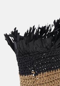 Zbliżenie na pleciony brązowo-czarny kapelusz ze słomy z frędzlami na czarnych krawędziach na białym tle.