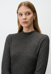 Grauer Wollpullover mit hohem Kragen und langen Ärmeln. Der Stoff ist weich, hat eine glatte Textur und keine sichtbaren Muster.