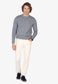 Suéter de lana gris con cuello redondo, combinado con pantalones color crema y zapatillas negras con suela de goma. Detalle sencillo del logotipo en el suéter.