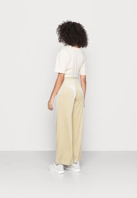 T-shirt cropped creme emparelhado com calças largas de veludo amarelo claro, apresentando uma faixa na cintura e riscas brancas; sapatilhas brancas.