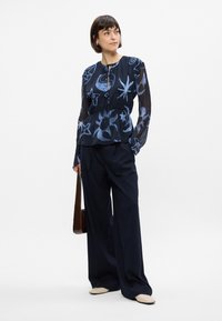Blouse en voile bleu marine avec des motifs d'étoiles et de lunes bleu clair, taille cintrée ; associée à un pantalon large à rayures bleu marine et des chaussures plates beiges.