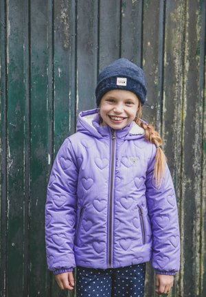 Lila gewatteerde jas met hartpatronen, ritssluiting en zijzakken, gedragen over donkerblauwe broek met kleine witte harten, en afgewerkt met een donkerblauwe beanie.