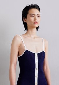 Vestido de punto en azul marino con ribetes blancos y tirantes ajustables. Presenta un cierre frontal con botones redondos.