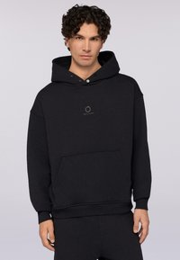 Černá mikina s kapucí a přední kapsou, vyrobená z měkké tkaniny. Obsahuje ozdobný logo prvek a žebrované manžety na rukávech a lemu.