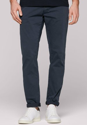 Marineblaue Baumwoll-Chinos mit schmaler Passform und hochgekrempelten Säumen, kombiniert mit weißen Sneakern. Weiche Textur und minimalistisches Design.