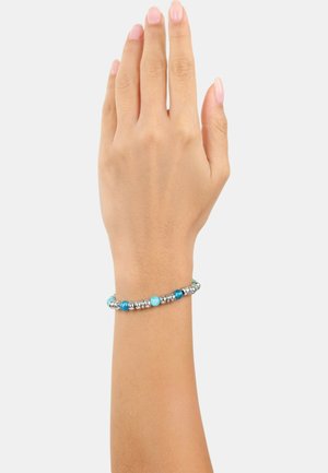 Bracciale con perline caratterizzato da metallo in tono argento e varie perle blu su un cinturino flessibile, mostrato su una mano di tono della pelle su uno sfondo bianco.