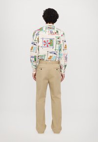 Langarmhemd mit bunten, strandthemen Prints, aus Baumwollstoff. Kombiniert mit beigen, locker sitzenden Hosen mit Gesäßtaschen.