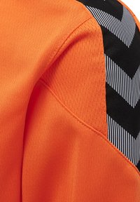 Oranges Sporthemd aus Stoff mit strukturierten Abschnitten, featuring ein schwarzes Paneel mit weißen diagonalen Streifen und einem Chevron-Muster auf der Schulter.