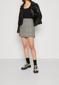 Osoba oblečená v černém topu bez rukávů, černé kožené bundě, mini sukni z černo-bílé tkaniny, černých ponožkách a třpytivých stříbrných platformových botách.