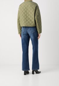 Olivengrøn quiltet jakke med en cropped design, parret med blå vide jeans. Sorte hæle støvler fuldender outfittet.