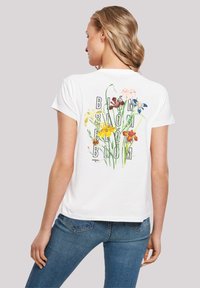 Witte katoenen T-shirt met een bloemenprint met verschillende kleurrijke bloemen en het woord "BLOOM" in vette, zwarte letters op de achterkant.