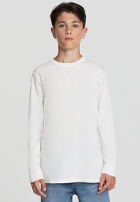 Biała koszulka z długim rękawem i okrągłym dekoltem, wykonana z miękkiego materiału. Noszona z niebieskimi dżinsami, o prostym kroju i lekkim zużyciu.