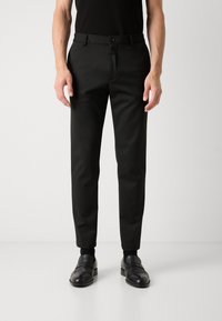 Black tailored trousers with a slim fit, flat front, belt loops, and a smooth texture. Paired with shiny black loafers.