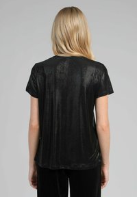 Haut noir à manches courtes en tissu brillant et texturé ; coupe ample ; ourlet légèrement courbé ; sans motifs ni détails en métal visibles.