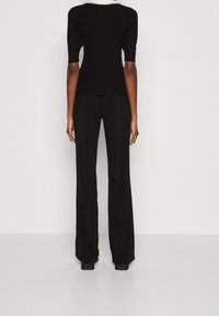 Haut en maille côtelée noire avec manches courtes bouffantes, associé à un pantalon noir à jambes larges et taille haute. Texture lisse, design minimaliste.