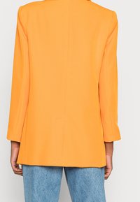 Blazer in bright orange, made of smooth fabric, featuring a tailored fit and long sleeves, with a vented back and minimal detailing.