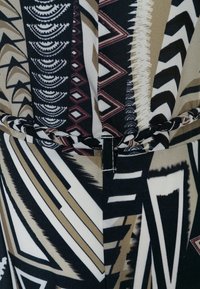 Mångfärgad klänning med tribal-mönster i svart, vitt, beige och vinröd. Tyget har en slät textur och en knuten detalj.
