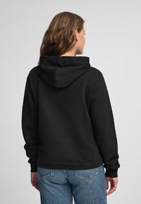 Felpa nera con cappuccio, dal taglio rilassato, con polsini e orlo a coste. Tessuto morbido e cuciture pulite, abbinata a jeans di denim blu chiaro.