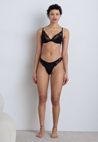 Soutien-gorge noir avec dentelle et culotte assortie, présentant un tissu doux, des accents en dentelle délicats et un design élégant sur fond neutre.