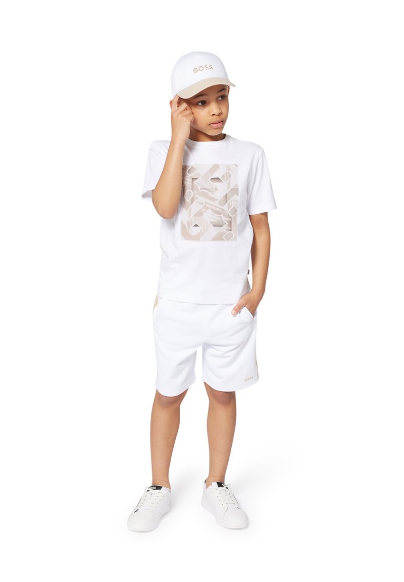 T-shirt blanc avec un motif géométrique beige, shorts blancs et baskets blanches. Une casquette blanche avec le logo "BOSS" complète l'ensemble.