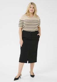 Beige gestreepte trui met korte mouwen, gecombineerd met een zwarte kokerrok met een split aan de voorkant, en zwarte puntige hakken.
