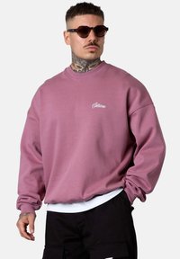 Pink crew neck sweatshirt with ribbed cuffs and hem, featuring a small embroidered logo on the chest. Comfortable, relaxed fit.