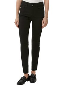 Jean skinny noirs avec une taille haute, deux poches avant, fermeture à bouton et une texture lisse et extensible. Associés à des mocassins noirs.