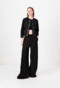 Giacca di jeans nera con ricami floreali sul davanti, abbinata a un top nero corto e pantaloni neri larghi con tasche laterali.