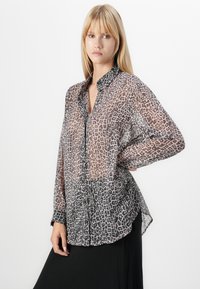 Camisa transparente com botões apresentando um padrão de leopardo em tons de castanho e preto, tecido leve, mangas compridas e bainha curvada.