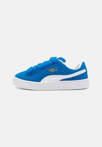 Zapatillas de ante azul con suela de goma blanca y detalles en blanco, con cordones prominentes y marca en el costado. Parte superior texturizada para mayor agarre.
