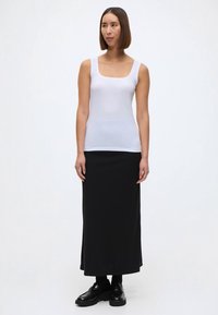 Balts bezpiedurkņu augšdaļa ar kvadrātveida izgriezumu, kombinēta ar melnu, līdz grīdai garu svārku. Apģērbu papildina melnas kurpes un vienkāršs dizains.