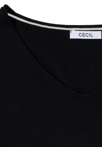 Haut en maille noir à col en V avec un bord intérieur rayé blanc et noir et une étiquette de marque "CECIL" cousue à l'intérieur.