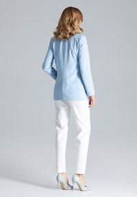 Jasnoniebieska marynarka o dopasowanym kroju, zestawiona z białymi spodniami wąskimi i jasnoniebieskimi szpilkami. Gładka tekstura materiału.