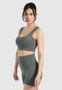 Conjunto deportivo verde que incluye una camiseta ajustada sin mangas y pantalones cortos de tiro alto, fabricado en una tela suave y elástica con costuras mínimas.