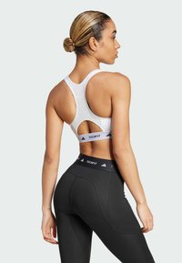 Hvit sports-bh med utskjæringsdesign og svart merkevare, kombinert med høyhårede svarte tights med teksturerte paneler og logo-linning.