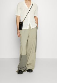Camisa de punto blanca de manga corta con un patrón de diamantes, combinada con pantalones sueltos en tonos beige y gris a rayas y zapatos negros tipo deslizante.