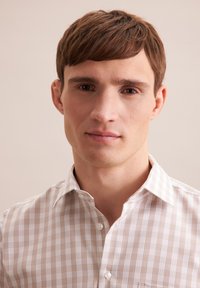 Camicia bianca con motivo a quadri marrone chiaro, design con bottoni e colletto standard. Tessuto morbido, indossata in evidenza da un modello maschile.