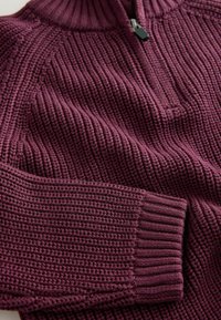 Pull en maille de couleur bordeaux foncé, avec un col montant, une fermeture éclair sur le devant et des poignets côtelés. Motif épais et texturé sur l'ensemble.