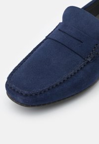 Mocassins en cuir suédé bleu marine avec un bout arrondi, des coutures le long des bords et une petite section surélevée à l'avant.