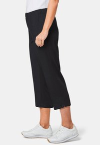 Zwarte cropped broeken met een elastische tailleband, voorzien van zijsplitten, gecombineerd met witte sneakers. Glad materiaal, getailleerde pasvorm.