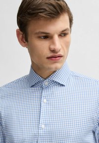 Jasnoniebieska koszula w kratkę, krótki kołnierzyk, z zapięciem na guziki, wykonana z tkaniny w splot, z drobnym wzorem w gingham i gładką fakturą.