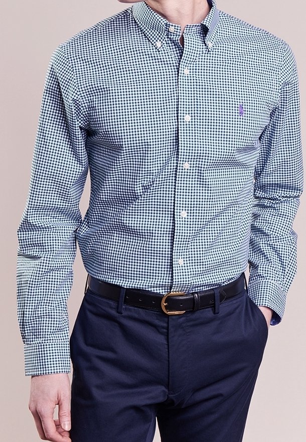 Grön och marinblå rutmönstrad skjorta med knappar, spetshals, långa ärmar och en liten logotyp på bröstet, i kombination med mörka byxor.