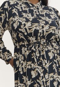 Mörkblå skjortklänning med vit och senapsfärgad blommönster, knäppning fram, långa ärmar, elastisk midja och knytband detaljer.