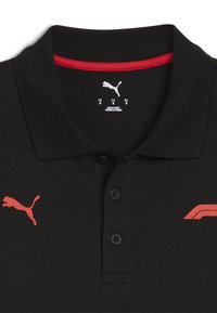 Čierna polokošeľa s rebrovaným golierom, s červenými akcentmi a malým červeným logom. Má dva čierne gombíky na prednej strane.