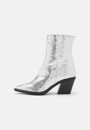 Silberne Stiefeletten mit strukturiertem, metallischem Finish, spitzem Zehenbereich und schwarzem Blockabsatz. Die Oberfläche weist ein reptilieninspiriertes Muster auf.