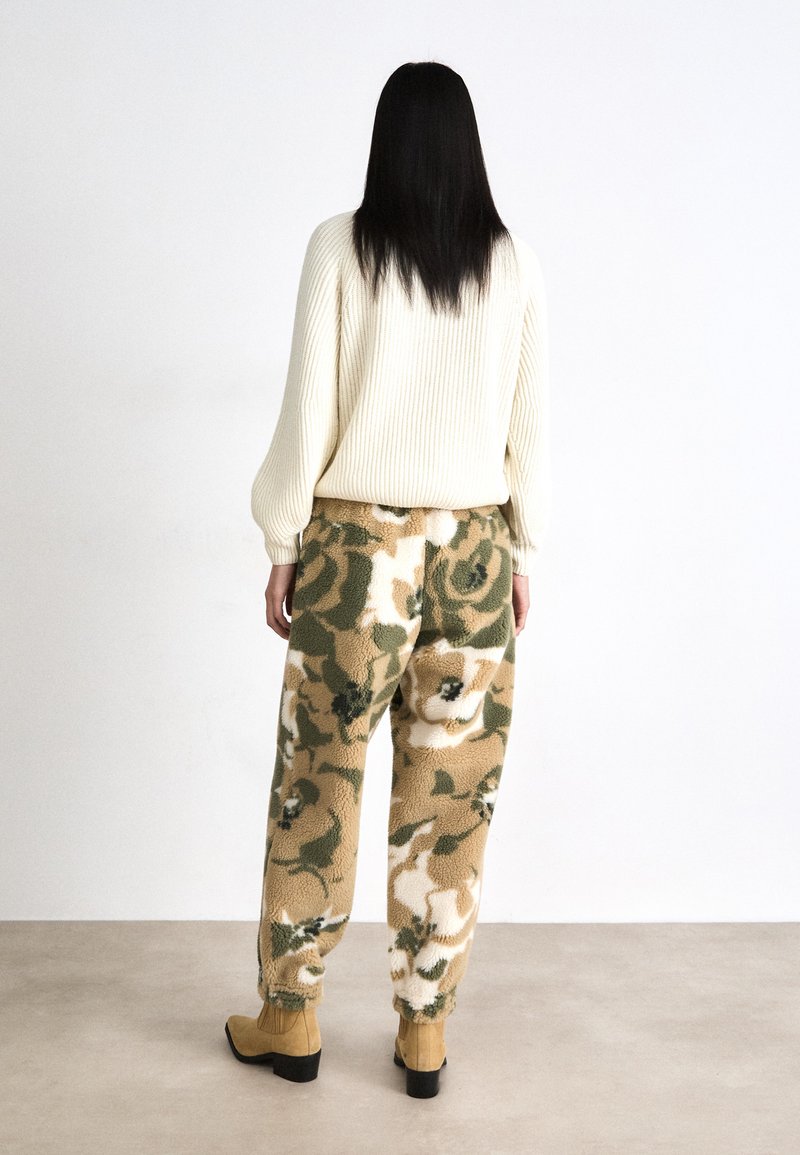 Sweter w kolorze kremowym, wydziergany, oraz fuzzy, wzorzyste beżowe i zielone spodnie z kwiatowymi akcentami, połączone z brązowymi botkami na obcasie.