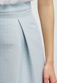 Gonna azzurro chiaro con tessuto strutturato con un delicato motivo floreale, dettaglio a pieghe e vita aderente.