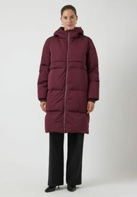 Burgunderfarget puffjakke med hette, med horisontale sømmer og hel frontglidelås. Kombinert med svarte vide bukser og høye hæler.