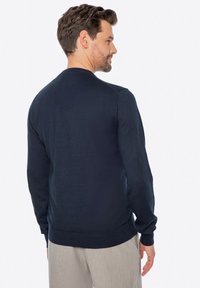 Granatowy sweter na okrągłym dekolcie z długimi rękawami, prążkowanymi mankietami i dołem. Gładka faktura i dopasowany krój, podkreślający czystą sylwetkę.